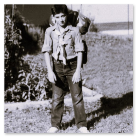 Vecchia foto in bianco e nero di un giovane Simone Mabellini (8-9 anni) in divisa da Lupetto scout con un grande zaino, pronto per un'uscita.